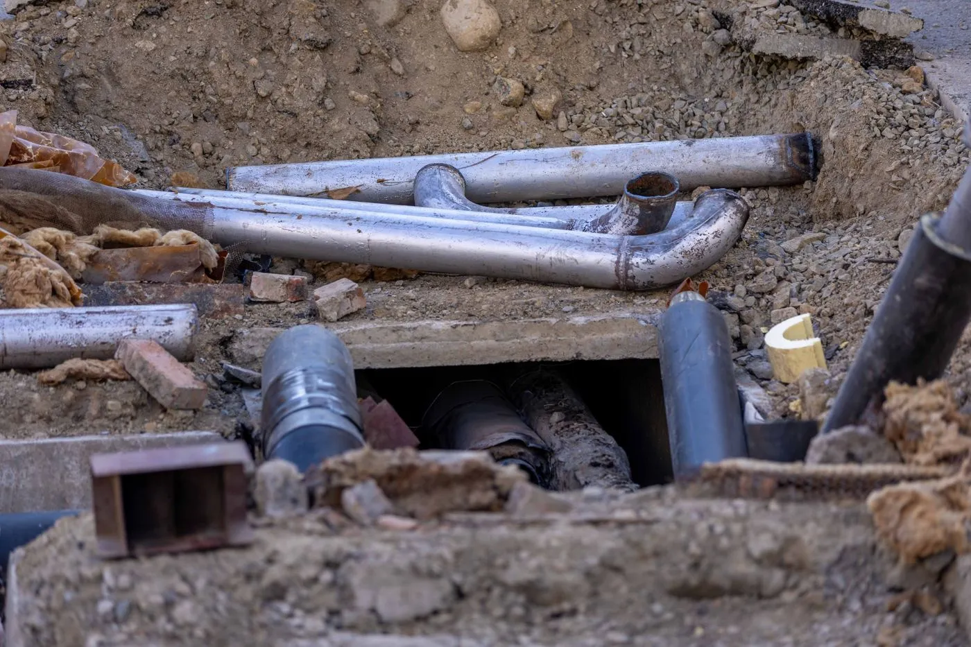 Canalisations mises à nu au fond d’une tranchée ouverte, terre et gravats autour